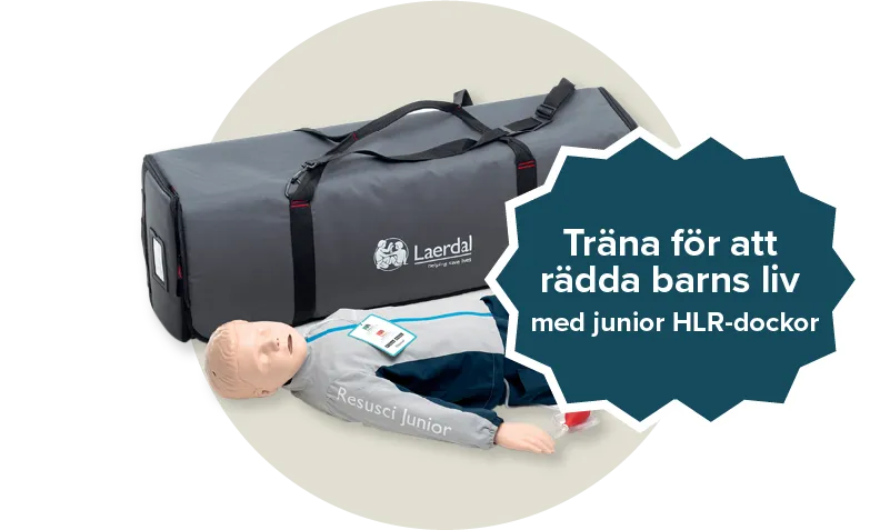 Resusci Junior QCPR docka med en grå och blå jacka. En grå väska från Laerdal. Etikett: Träna för att rädda barns liv med junior HLR dockor