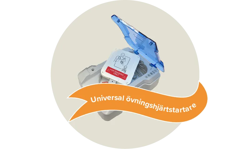 En grå övningshjärtstartare med ett blått genomskinligt lock från märket Prestan AED trainer. Etikett: Universal övningshjärtstartare.